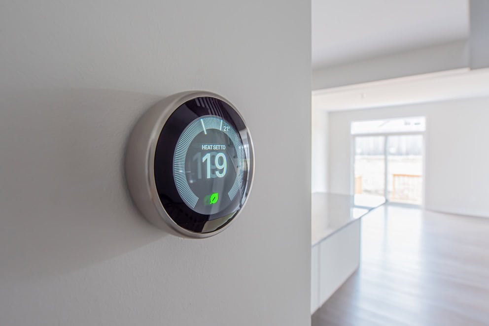 a simplistic photo of a round, modern, programmable digital thermostat, on a clean white wall in heating mode